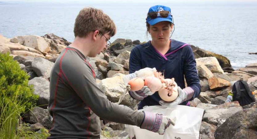 Two students pick up trash on a beach as part of a service project. 